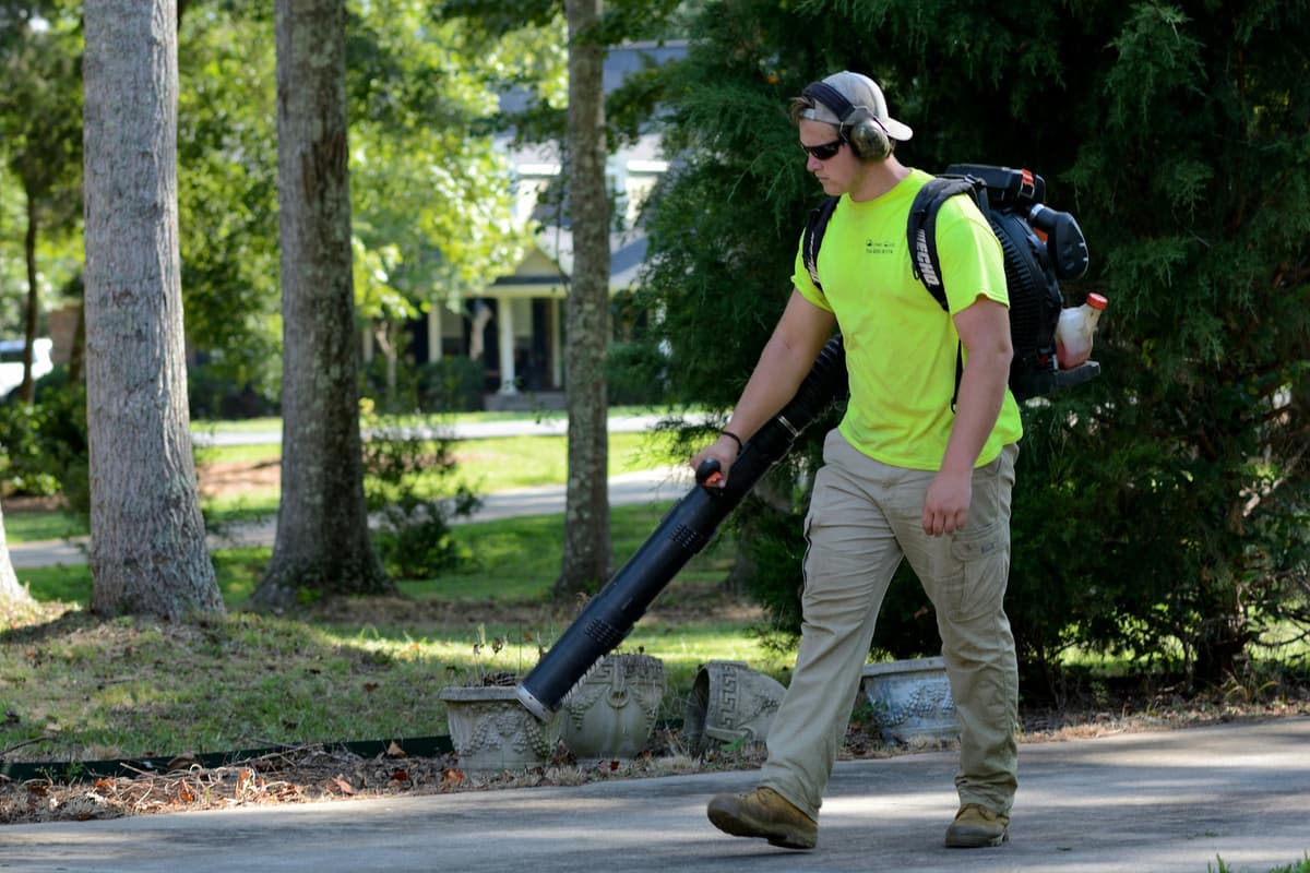 Worker clearing leaves from a driveway with a backpack blower